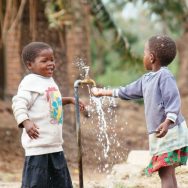 Two girls playing at a water tap
