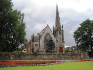 A picture of the Old Parish Church in Blantyre is displayed at an angle. The sky is cloudy and there are trees and a wall also in view.